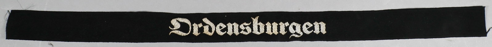 NS-ORDENSBURGEN TRAINING SCHOOL CUFF TITLE: A scarce NSDAP cuff title, 15 x 1 in., bevo-style construction of black rayon with the legend ‘Ordensburgen’ in silver thread. These cuff titles were worn by instructors of the ‘NS-O