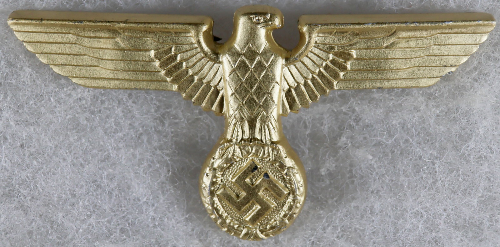 NSDAP EAGLE CAP BADGE BY C. DINSEL: An NSDAP political eagle cap badge, approx. 2.5 x 1.25 in., constructed of stamped aluminum with a gilt finish. The reverse is fitted with three crimped-in attachment prongs, and bears an RZM stamp ov