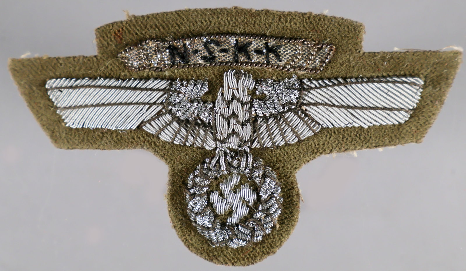NSKK EAGLE UNIFORM INSIGNIA: A hand-embroidered ‘Nationalsozialistisches Kraftfahrkorps (NSKK)’, or National Socialist Motor Corps uniform eagle insignia patch, approx. 3.5 x 2 in., of silver flat- and round-wire bull