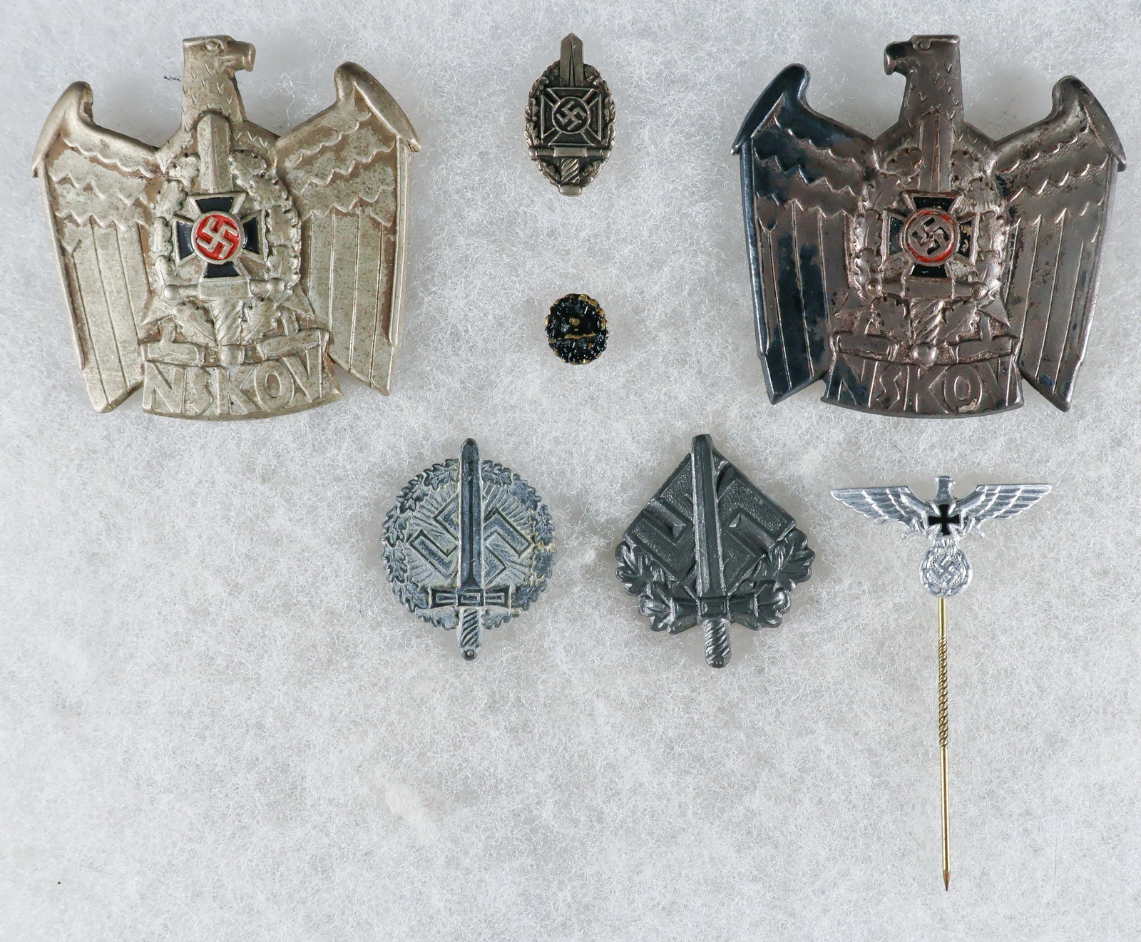 NSKOV CAP BADGES, VETERANS’ ASSOCIATION ‘SMALLS’: A good lot of seven pieces related to Third Reich-era veterans’ organizations, includes: two NSKOV cap badges, each approx. 1.75 in. square, the first a pin-back version RZM-marked