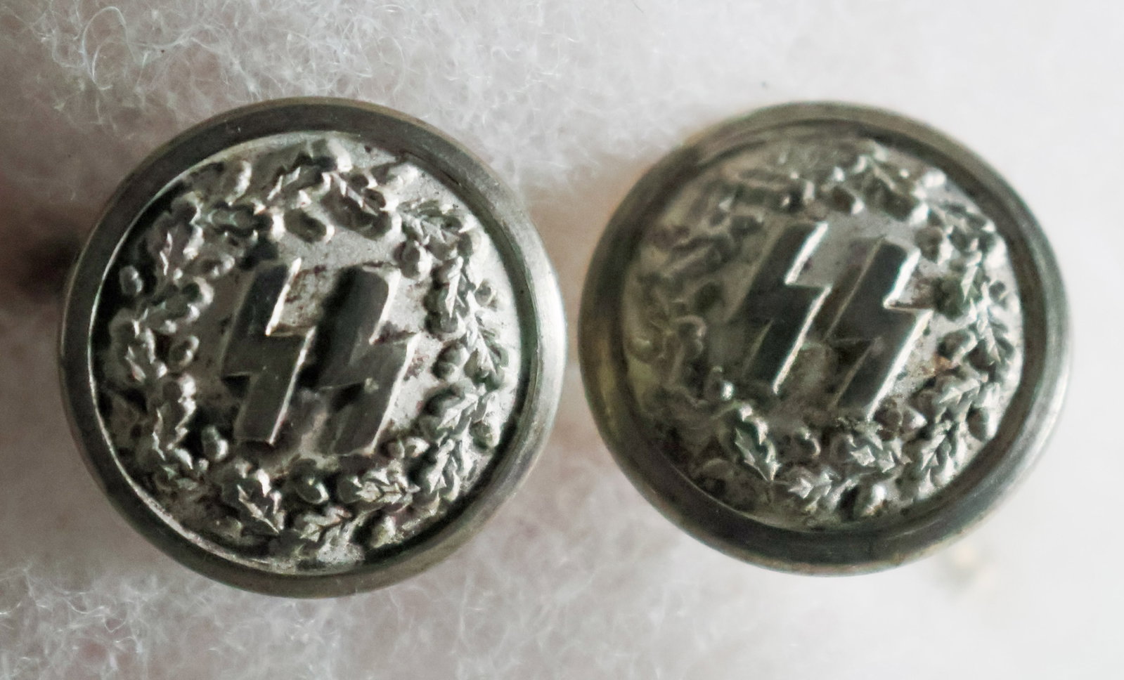 SS CUFFLINKS: A set of unmarked silver-toned cufflinks bearing SS runes with wreaths around them, the design and construction matches the buttons used on the SS mess dress uniform. Possibly from the same