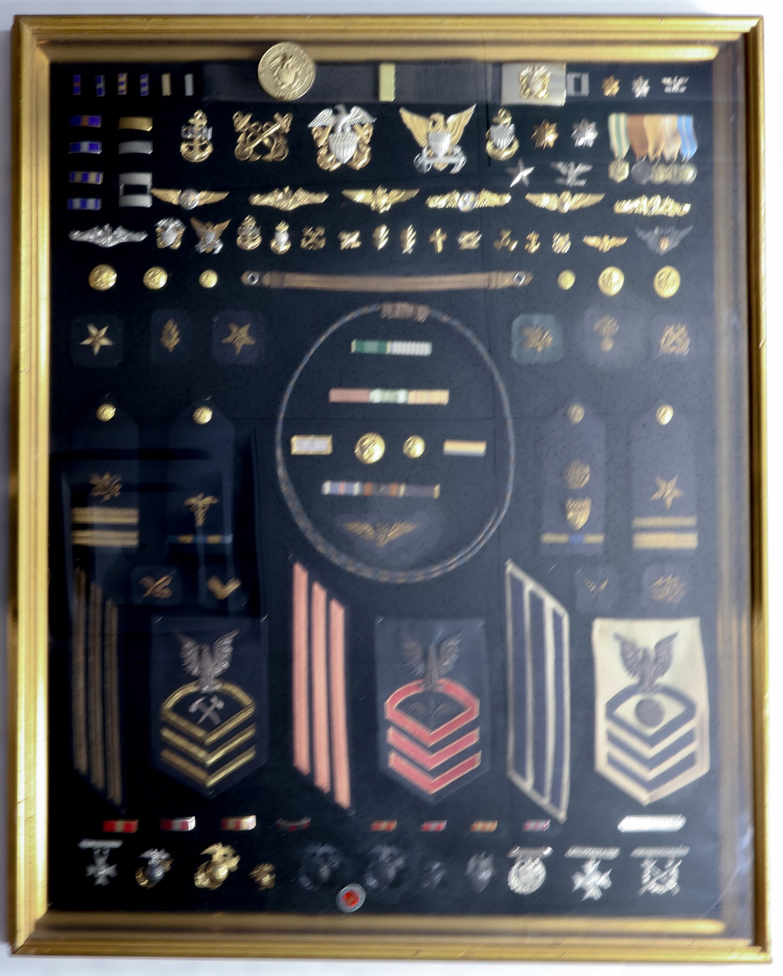U.S. NAVY AND MARINES FRAMED INSIGNIA DISPLAY: A beautiful display piece, fine fine collection of over one hundred different pieces of U.S. Navy and Marines insignia spanning over a century. A huge variety of insignia are present, including metal