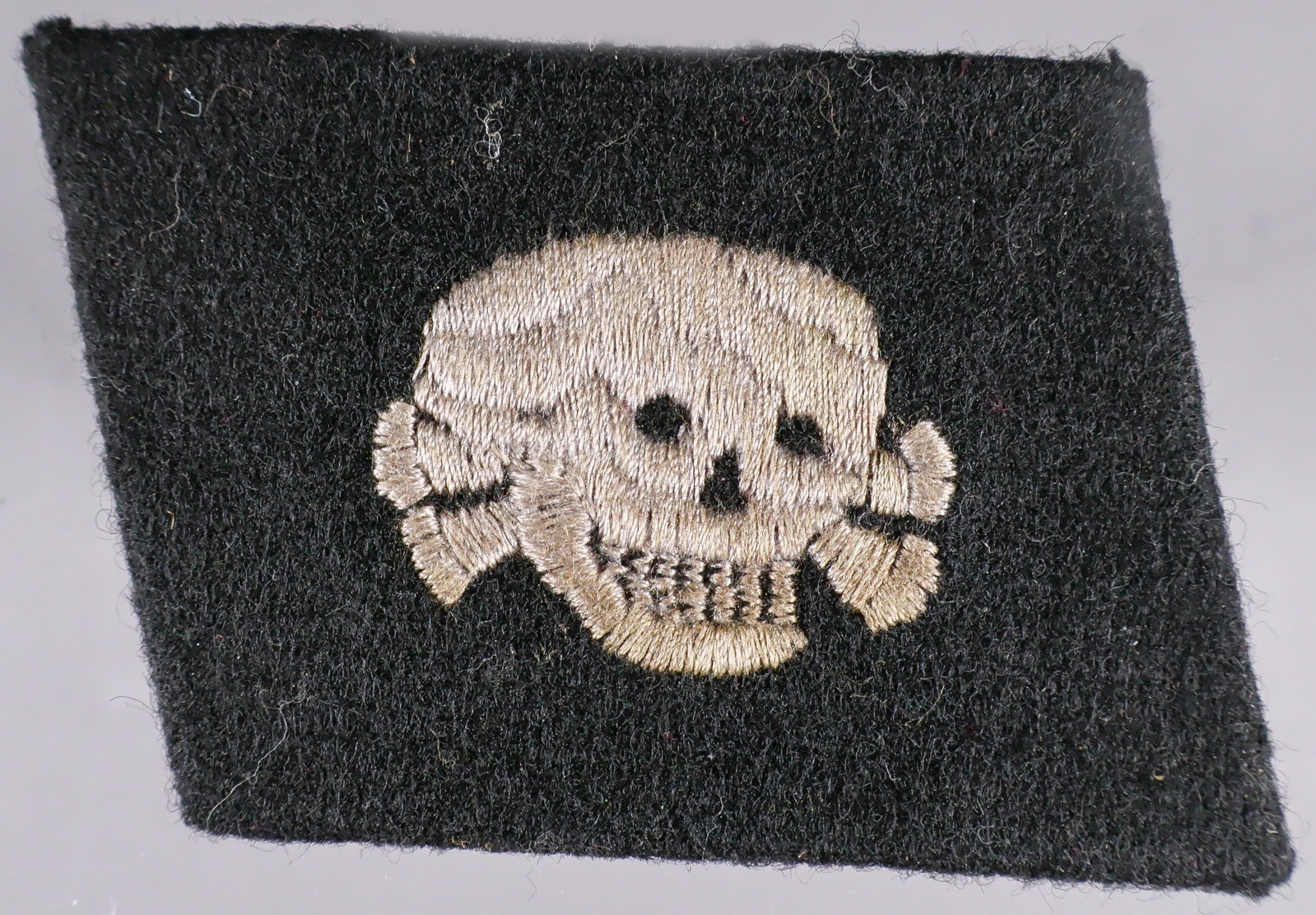 WAFFEN-SS 3RD PANZER DIVISION ‘TOTENKOPF’ COLLAR TAB: Horizontal-pattern Waffen-SS 3rd Panzer Division ‘Totenkopf’ collar tab, 2 x 1.5 in., constructed of black wool pasted over a brownish-gray buckram core, without piping, embroidered with