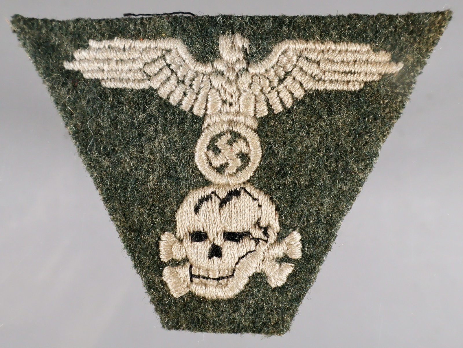 WAFFEN-SS M43 CAP INSIGNIA: A late-war Waffen-SS M43 cap insignia patch, 2.75 x 2 in., depicting an embroidered SS-style eagle and swastika over a ‘totenkopf’, all in silver thread with black thread accents to the