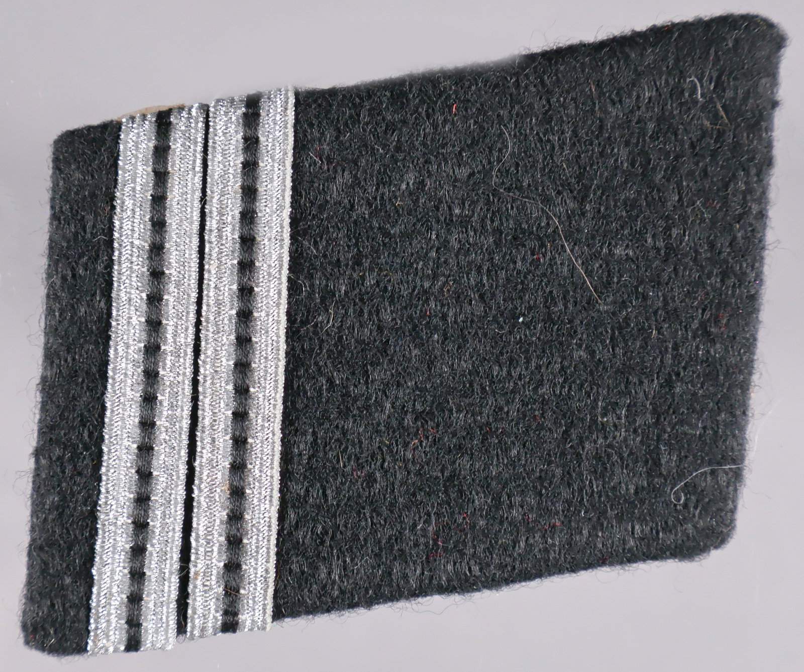 WAFFEN-SS ROTTENFUHRER’S COLLAR TAB: A wartime-made Waffen-SS rank collar tab, 2 x 1.5 in., constructed of black wool pasted over a brown buckram core, without piping, fitted with two bands of metallic silver with a black stripe,