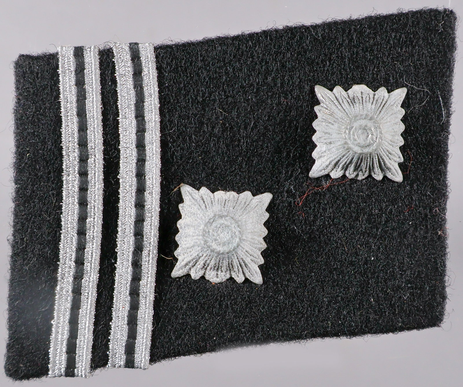 WAFFEN-SS STURMSCHARFUHRER’S COLLAR TAB: A wartime-made Waffen-SS rank collar tab, 2 x 1.5 in., constructed of black wool pasted over a brown buckram core, without piping, fitted with a two metal ‘pips’ over a two bands of