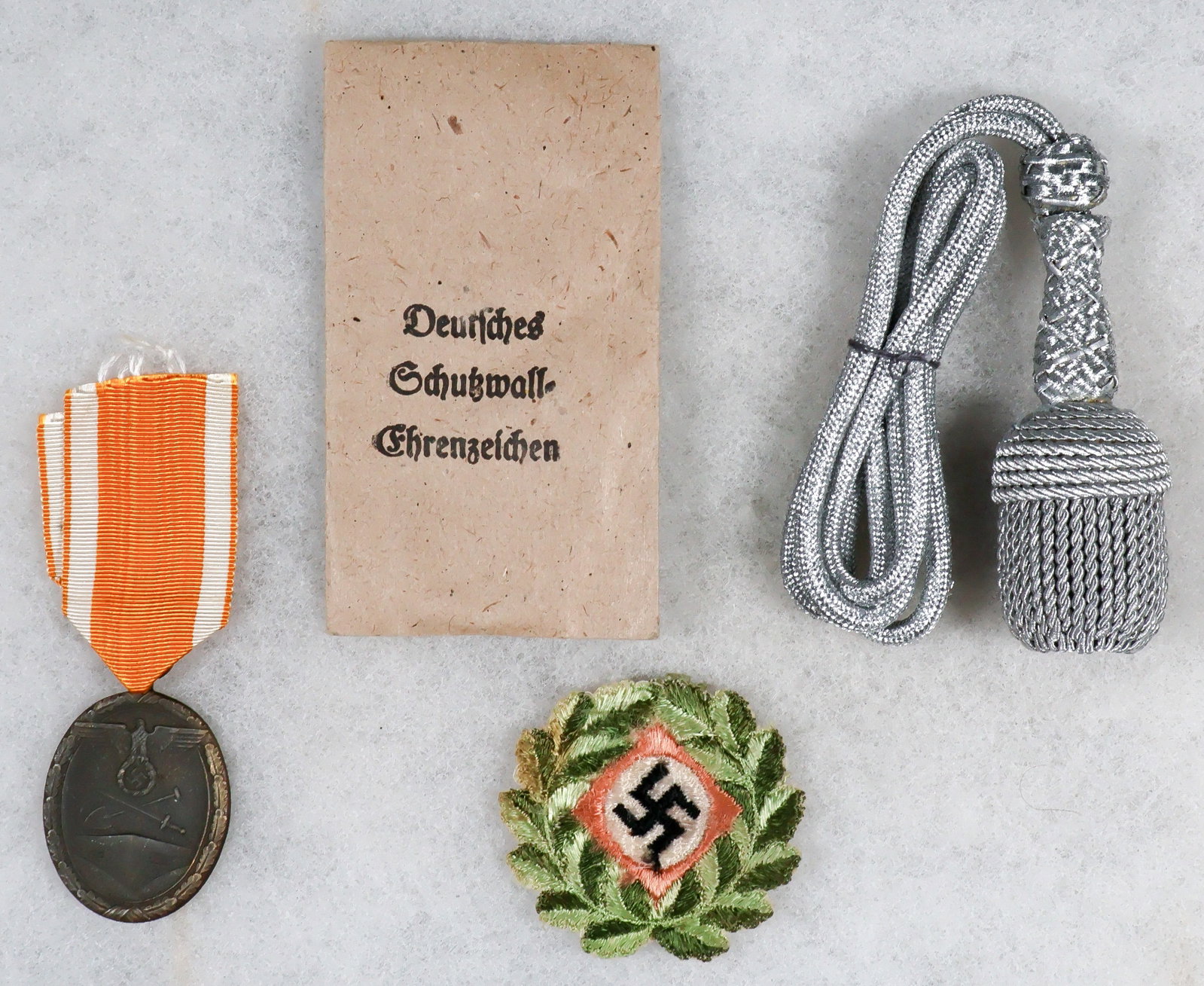 WEST WALL MEDAL, DAGGER PORTAPEE AND CAP INSIGNIA: A good lot of three Third Reich pieces, includes: a ‘Deutsches Schutzwall-Ehrenzeichen’, or West Wall Medal, with ribbon and original envelope, the latter marked by maker Carl Poellath.
