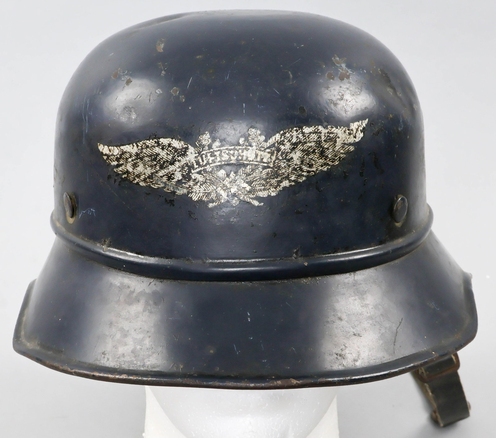 LUFTSCHUTZ HELMET: Black painted steel Luftschutz air raid helmet, chipped decal at front, original light brown leather liner and chinstrap, both in poor condition, the helmet itself bearing a few dents and chips. Just 