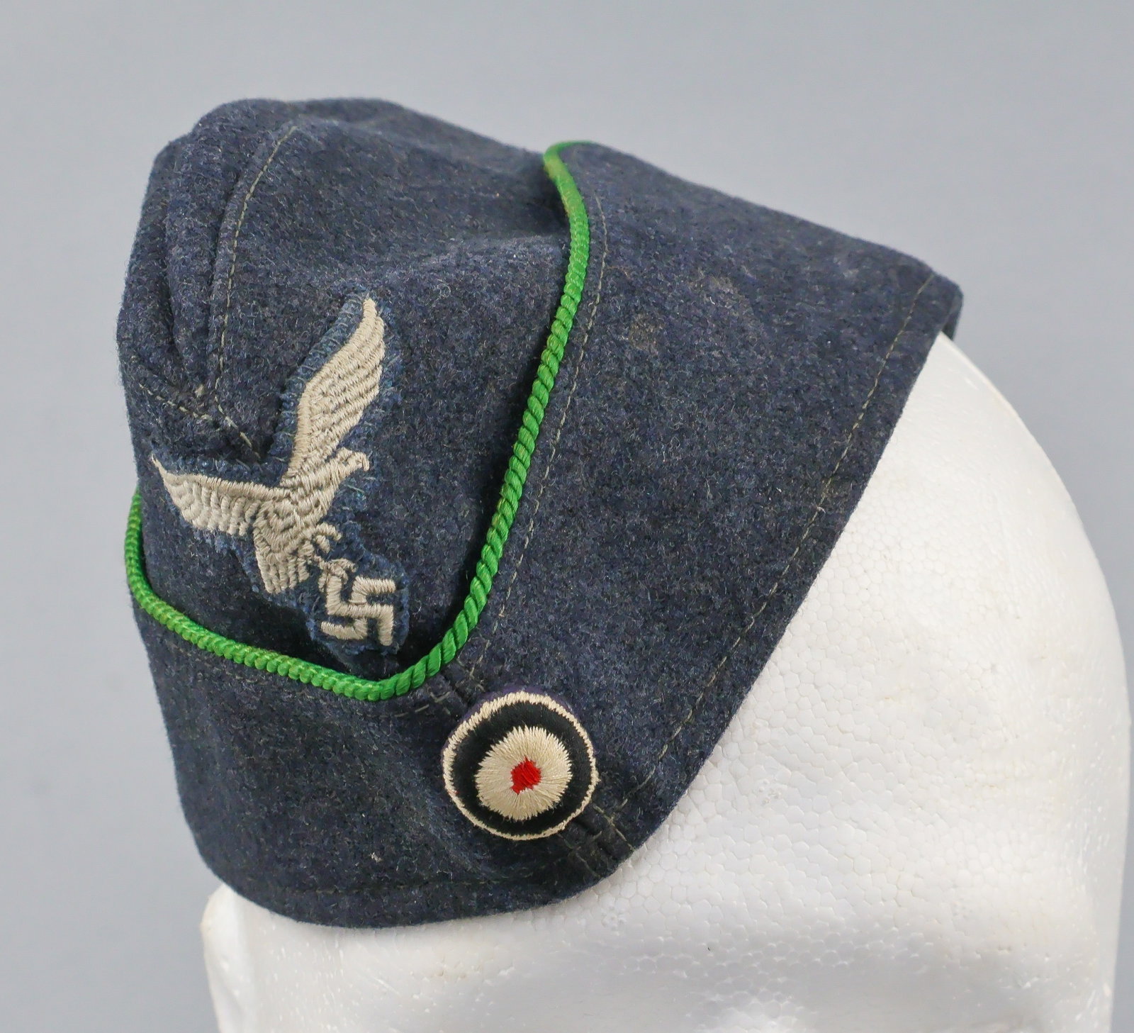LUFTWAFFE ADMINISTRATIVE PERSONNEL OVERSEAS CAP: Luftwaffe EM/NCO’s overseas cap, constructed of blue-gray blended wool and rayon, displaying a machine embroidered Luftwaffe patch at front center in pale gray cotton threads on a cut-out blue-g