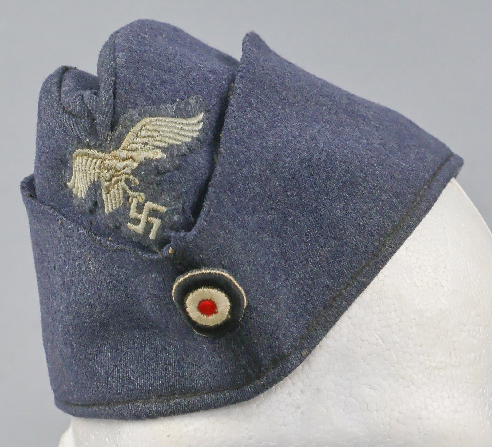 LUFTWAFFE OVERSEAS CAP: Luftwaffe EM/NCO’s overseas cap, constructed of blue-gray blended wool and rayon, displaying a machine embroidered Luftwaffe patch at front center in pale silver-gray cotton threads on a cut-out