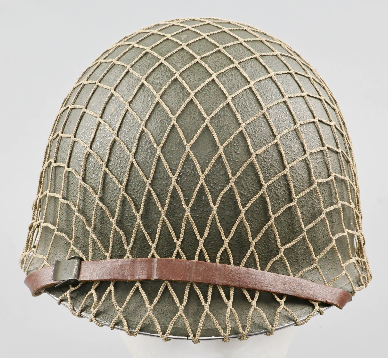 U.S. M1 FIXED-BALE HELMET: An early U.S. M1 steel combat helmet, the exterior finished olive-green with a corked texture, featuring a stainless steel rim with seam at the front. The chin strap bales are fixed, and secure a chin