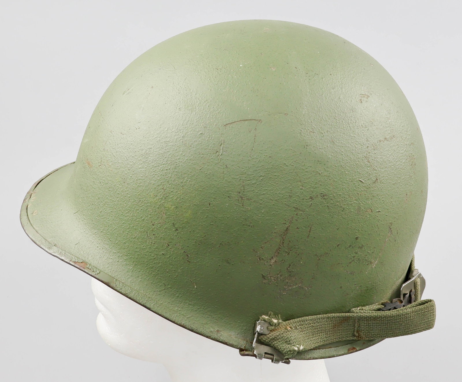 NAMED WORLD WAR II-MANUFACTURED M1 HELMET: A mid-World War II-manufactured U.S. steel M1 combat helmet, the exterior refinished olive-drab with a sand texture, featuring a stainless steel rim with seam at the front. The chin strap bales are of