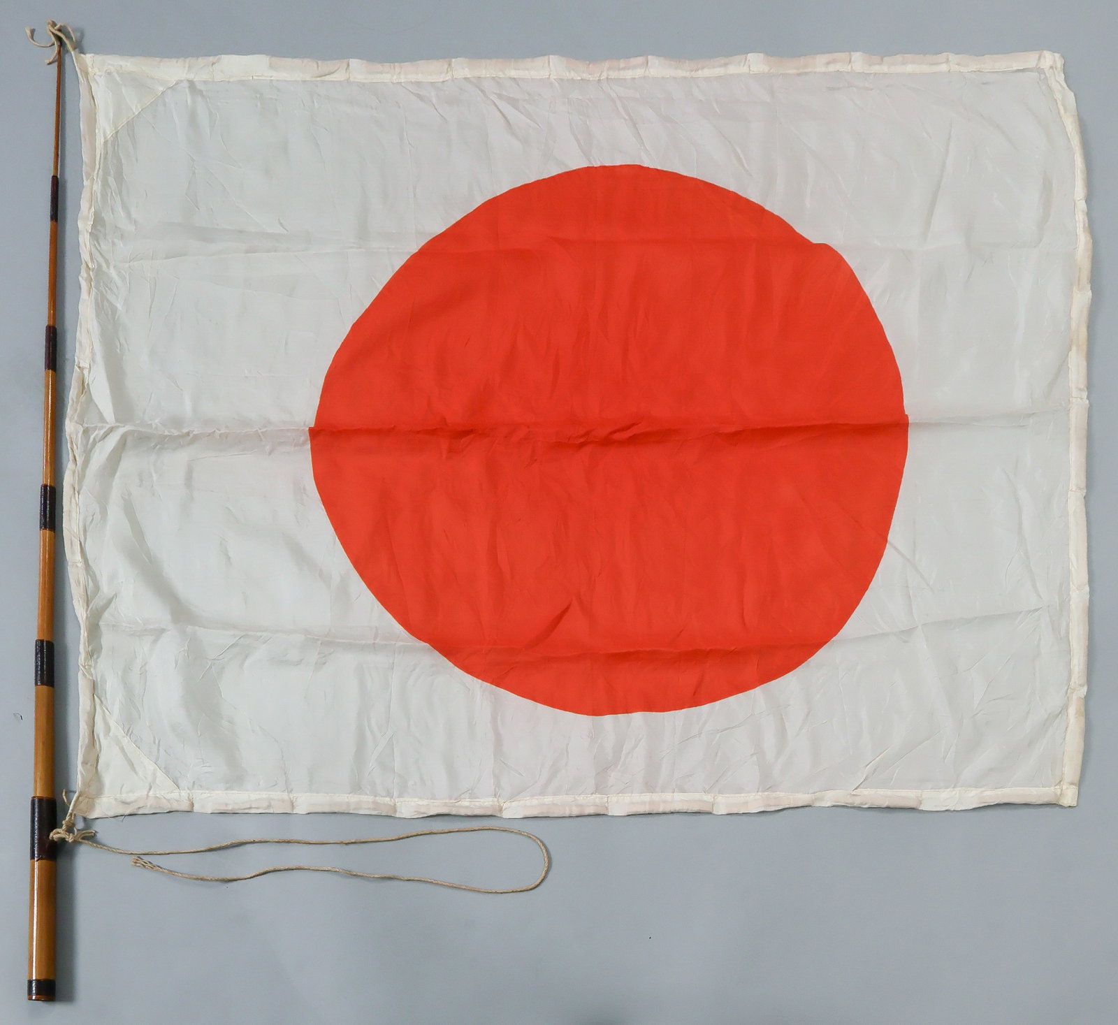JAPANESE PILOT’S SURVIVAL ‘FLOAT FLAG’: A rare Imperial Japanese pilot's silk survival ‘float flag', 39 x 31.5 in., a Japanese national flag with strips of kapok sewn into the edges, allowing the flag to float on the surface of the
