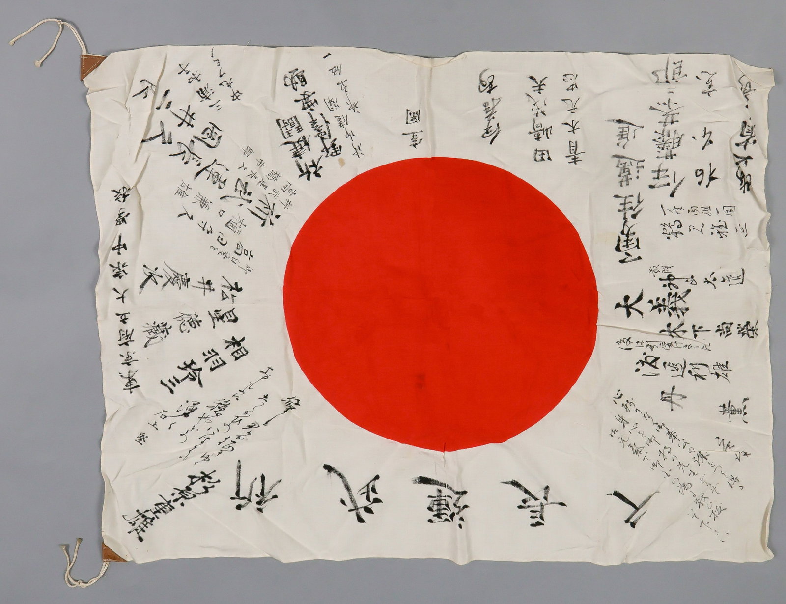 JAPANESE SOLDIER’S ‘GOOD LUCK’ FLAG: A cotton bunting Japanese national flag, 34 x 27.5 in., clamp-dyed with a red ‘rising sun’ at center, with the white field covered in Japanese inscriptions in black ink (untranslated),