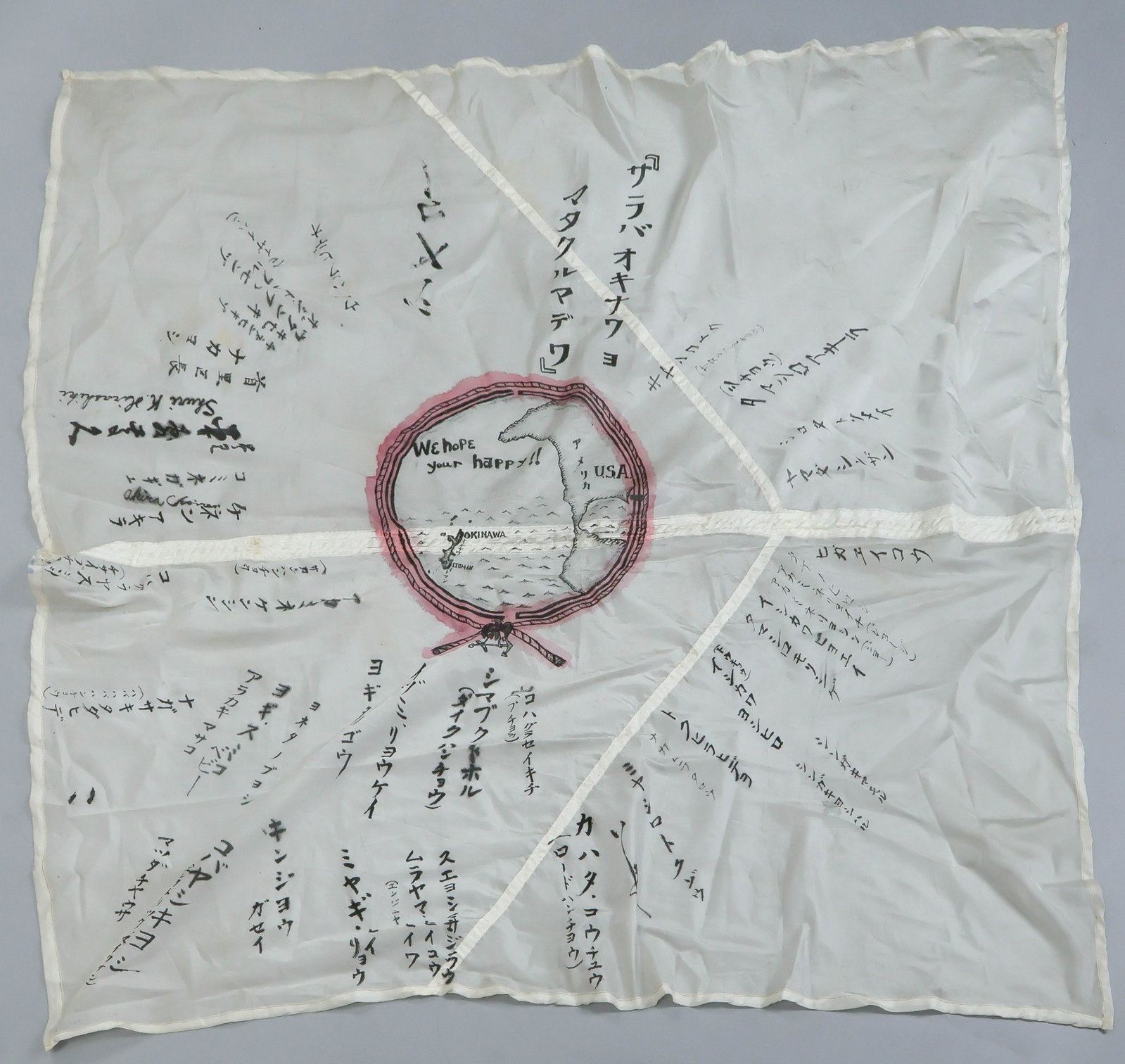 OCCUPATION OF OKINAWA SOUVENIR BANNER ON PARACHUTE SILK: A handmade souvenir of the American occupation of Okinawa, a banner constructed from a 45 x 43.5 in. section of silk cut from a Japanese parachute, with a hand-drawn illustration in ink at center