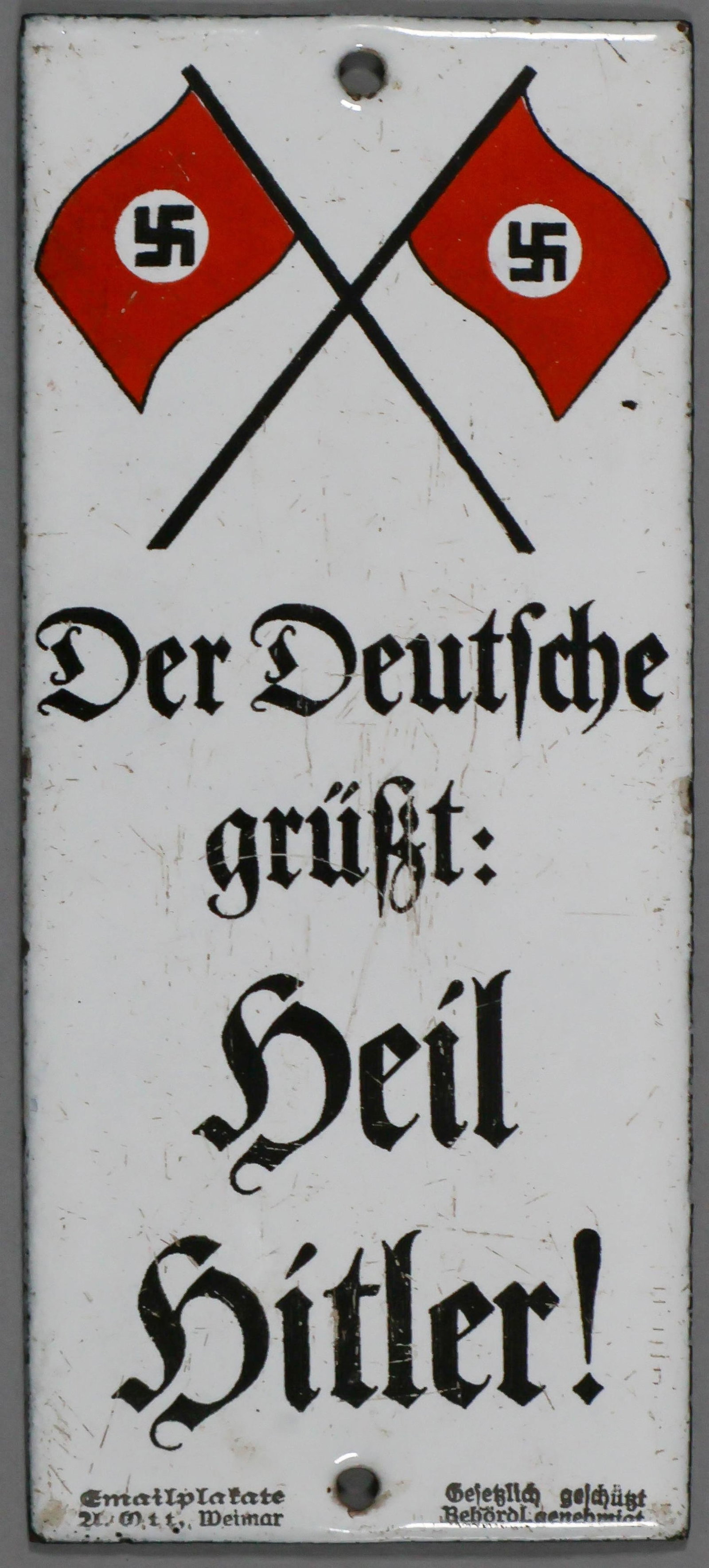 ‘THE GERMAN GREETS: HEIL HITLER!’ ENAMEL SIGN: A fascinating relic from the Nazi era, a white enameled sign, 2.5 x 6 in., featuring a Nazi and German national flag at the top, and reading ‘Der Deutsche Grusst: Heil Hitler!' (‘The