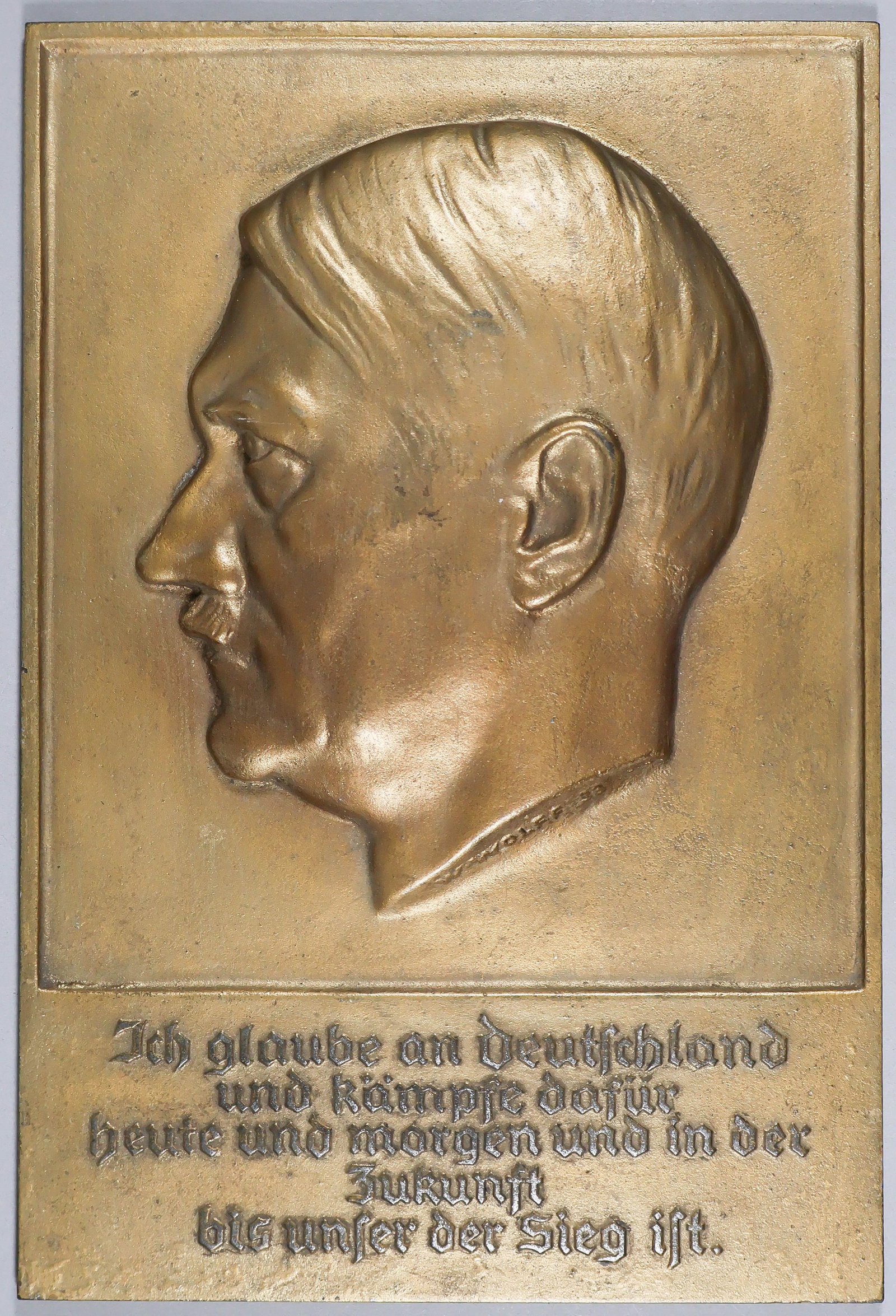 ADOLF HITLER PROFILE PLAQUE WITH QUOTATION: Heavy cast iron plaque with the left side profile of Adolf Hitler, 8.5 x 12.5 in. and signed by the artist 'W. WOLFF 33' at the base of the neck. The text reads 'Ich glaube an Deutschland und kampfe
