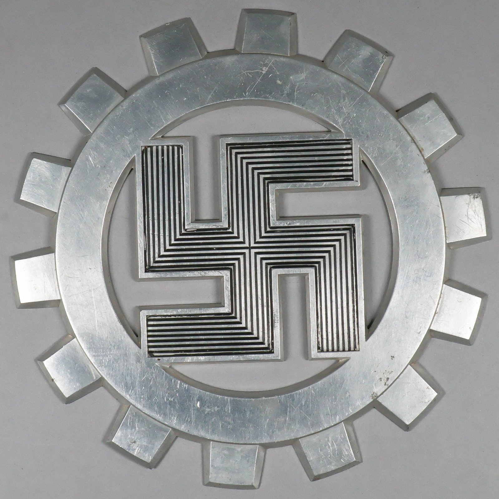 D.A.F. COG PLAQUE: An aluminum plaque, 8 in. dia., with the emblem of the ‘Deutsches Arbeitfront’, a detailed and mobile swastika, within a cog gear. It is not known for what purpose these plaques were