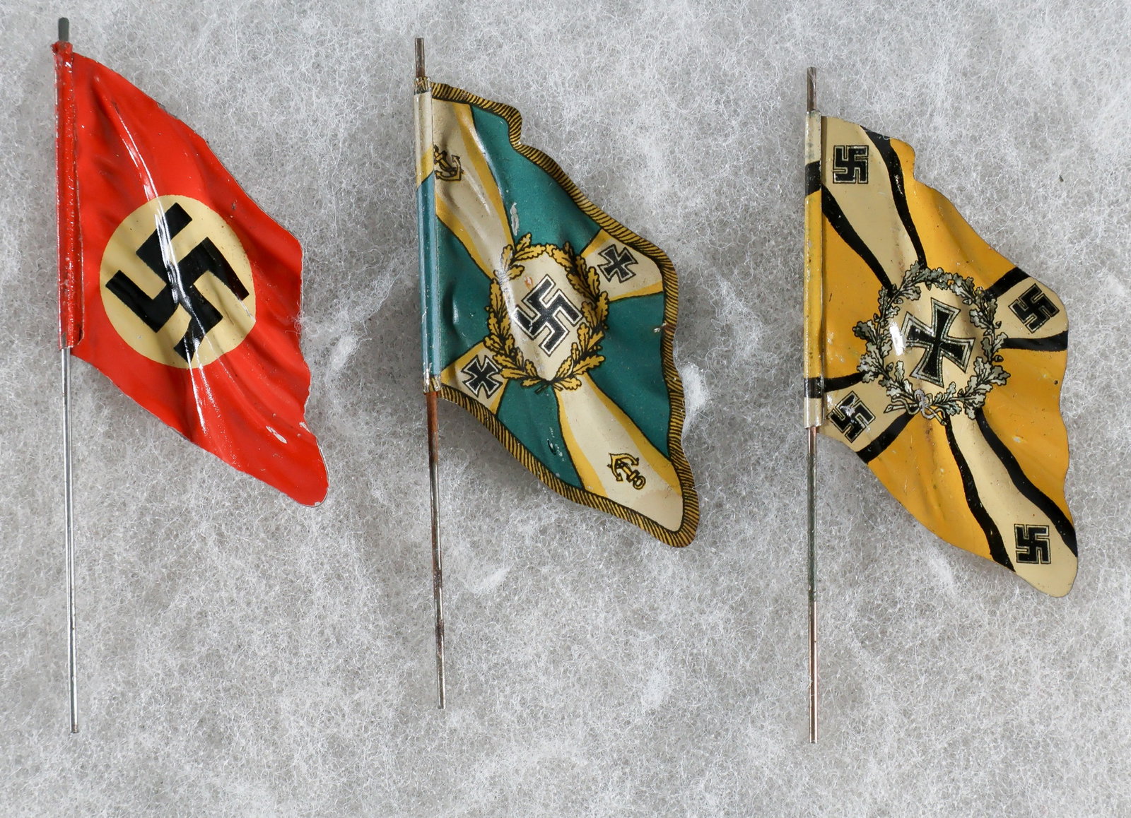 MINIATURE TIN NAZI FLAGS (3): A set of three enameled tin flags on pins measuring 3.75 in. long, the metal curled to evoke the feeling of them flying. The flags include the German national flag, green Kriegsmarine veteran’s