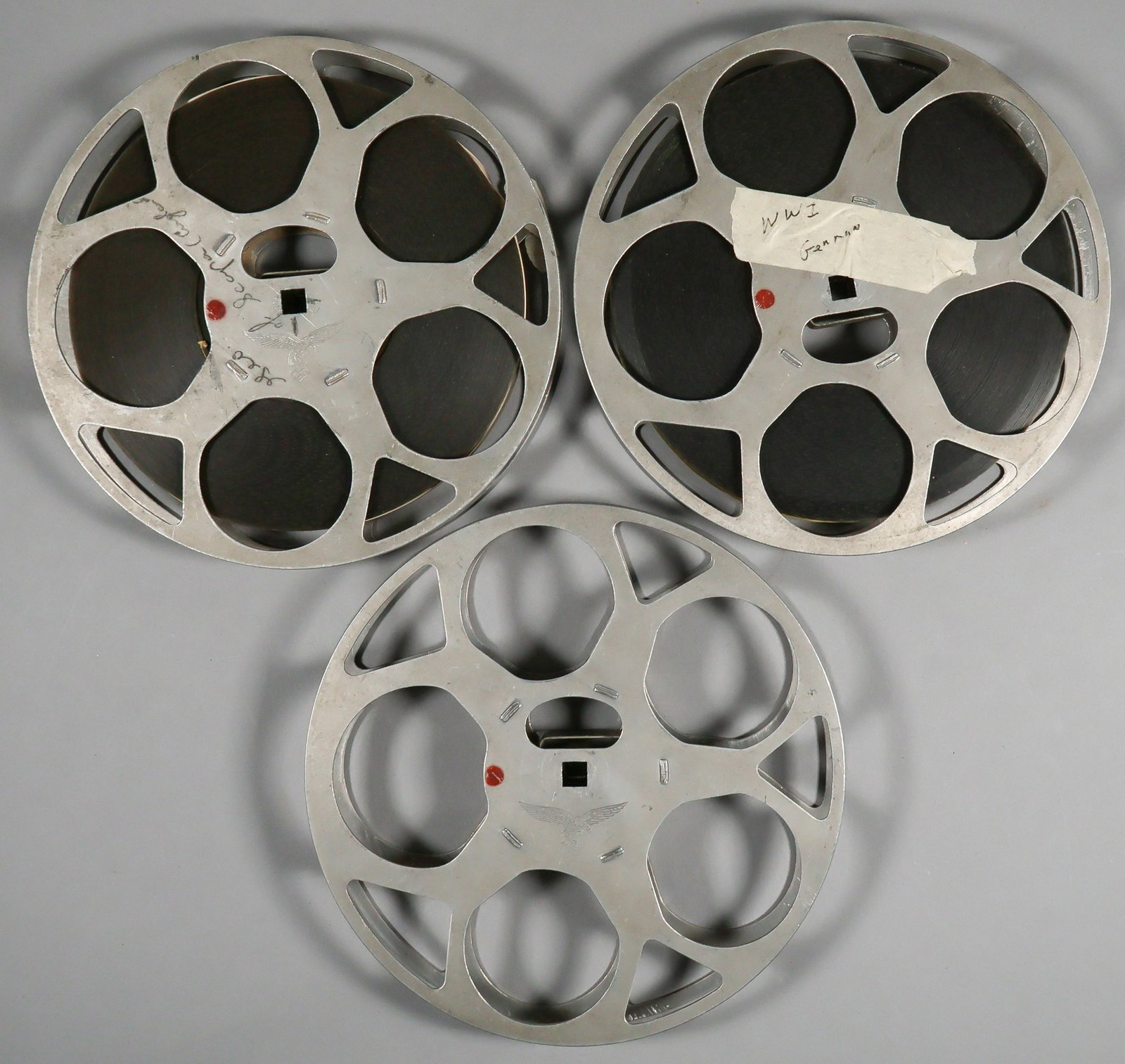 NSDAP 16MM REEL GROUP (3): Three 16mm metal film reels, 7 in. dia., all stamped with the NSDAP eagle at center. One bears a tape label reading 'WWI German' on one side and 'Hitler...' on the other. The second reel bears a note