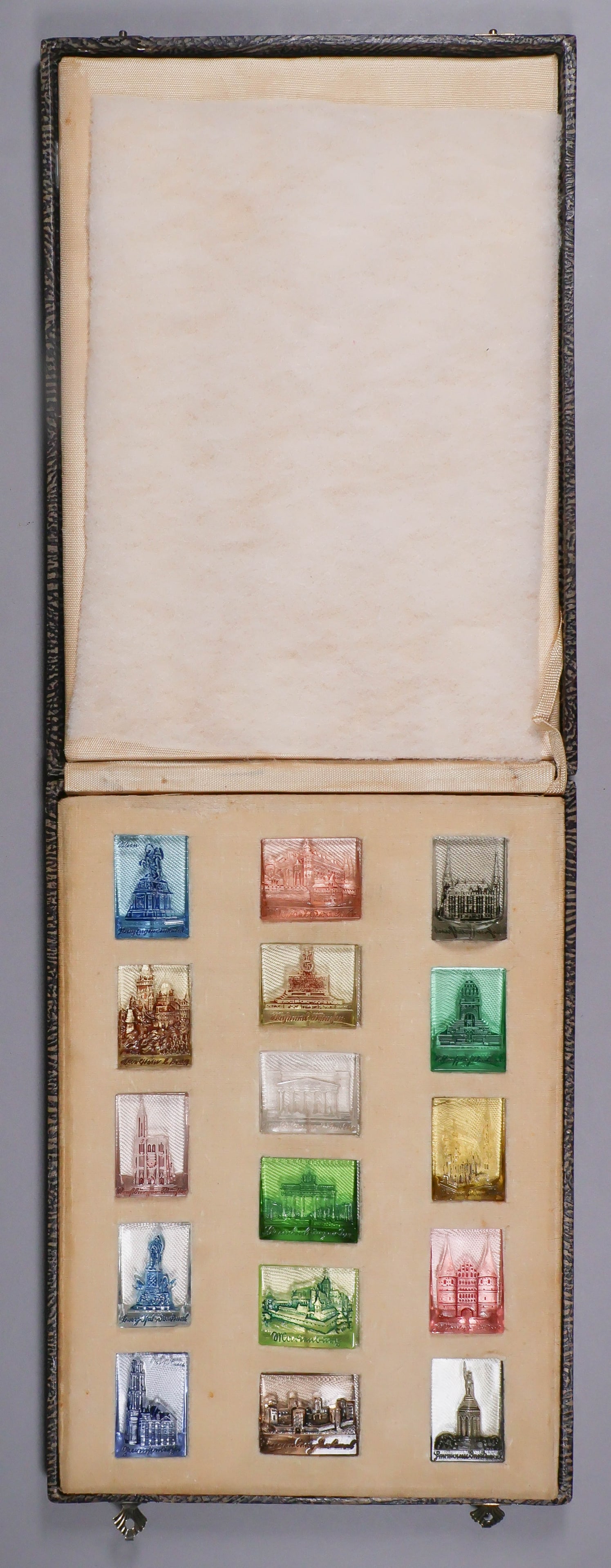 WINTERHILFSWERK BUILDINGS AND MONUMENTS GLASS MINIATURES: An unusual set of 16 souvenir molded glass plaques, ca. 1930s-1940s, each produced in a different color and with an image of famous German landmarks. The plaques, 1 in. x 1.33 in. to 1 in. x 1.5 in.,
