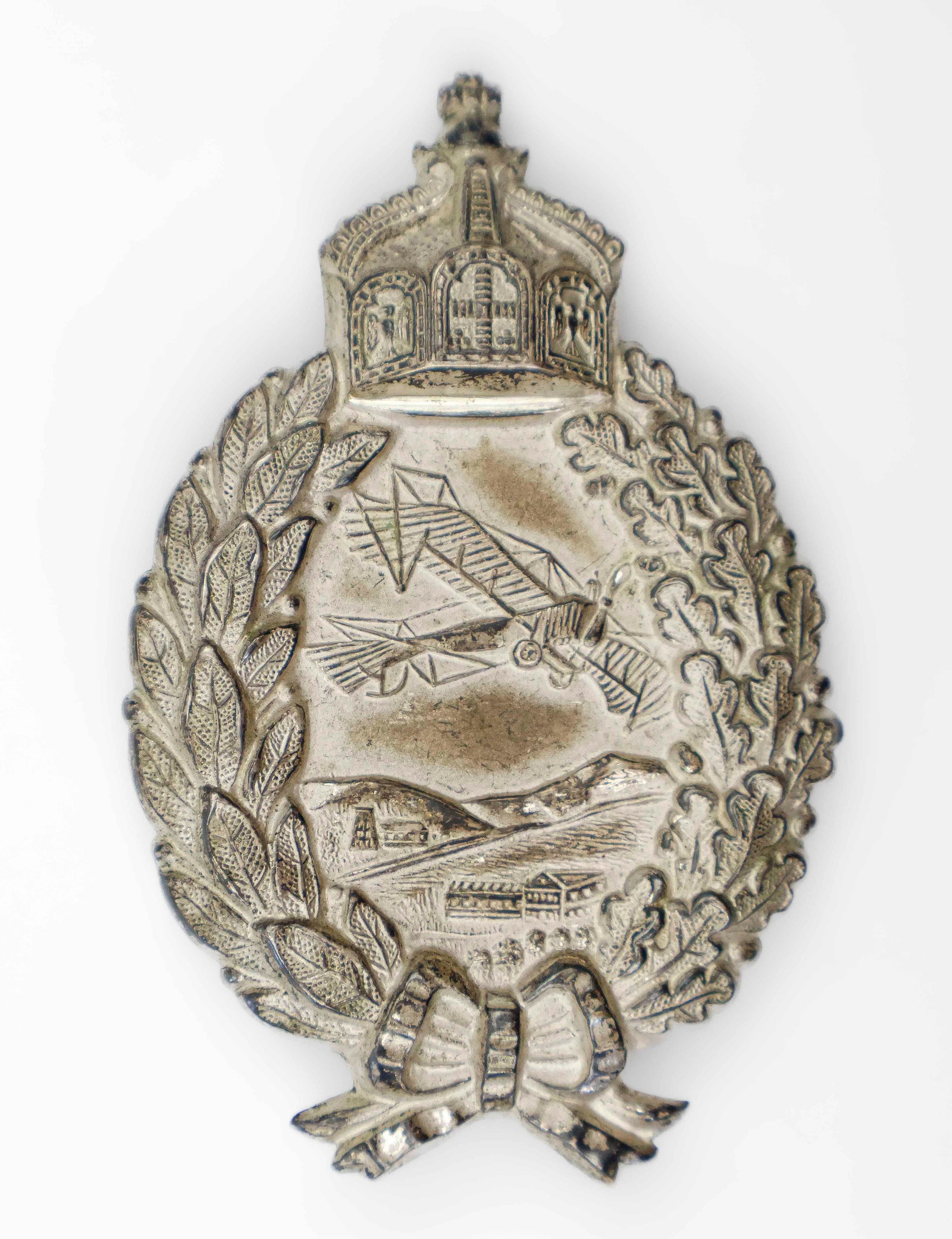 WORLD WAR I PRUSSIAN PILOT BADGE: A rare hollow back version of a Prussian Army Pilot Badge in die-struck silvered tombac, with fine details in high relief. It features an early-style plane soaring above the landscape, surrounded by a