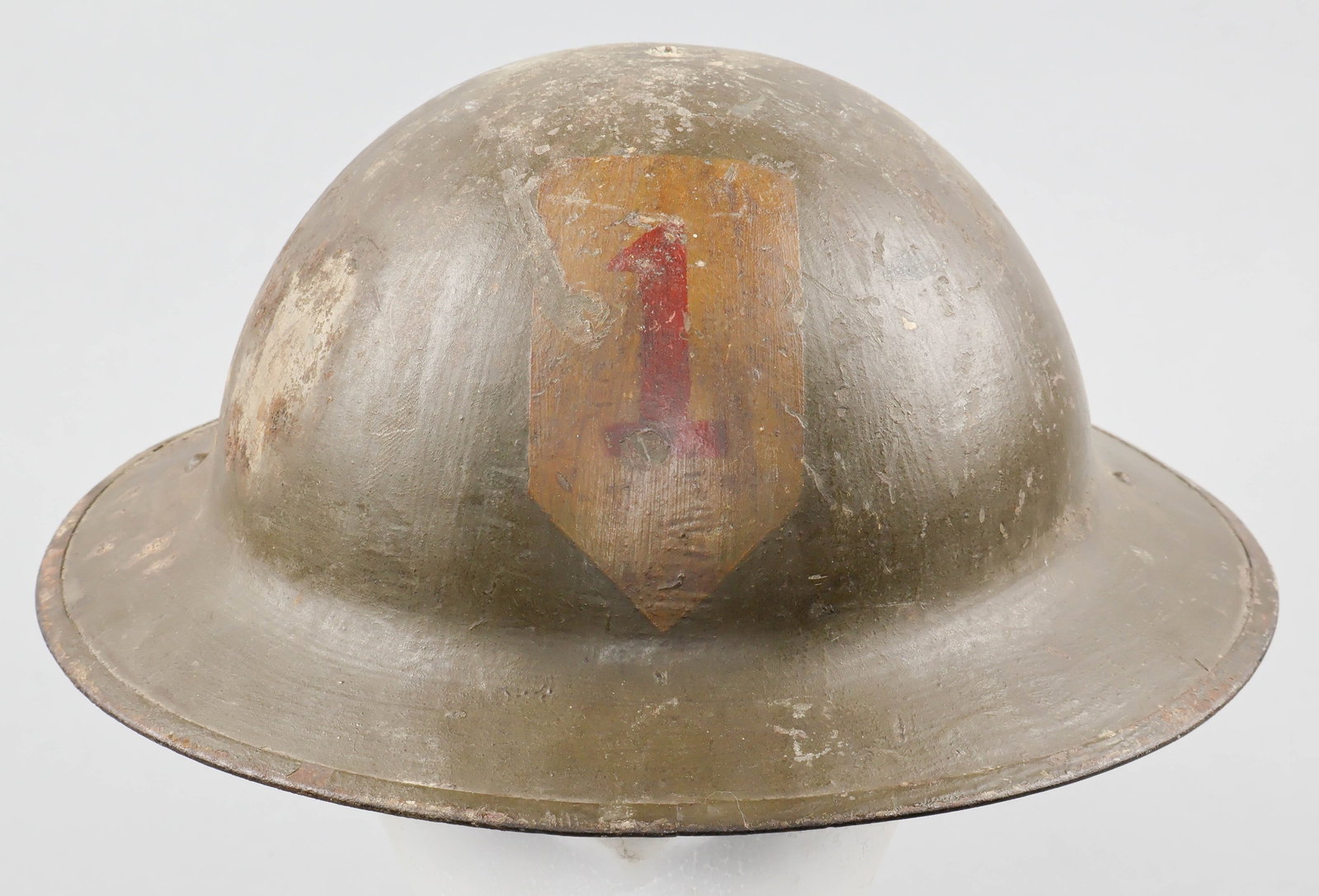 1ST INFANTRY DIVISION PAINTED M1917 HELMET SHELL: A fine example of a World War I U.S. soldier’s M1917 steel combat helmet, retaining its original green-brown sawdust-textured finish. Most notably, the front of the helmet displays the hand-pain