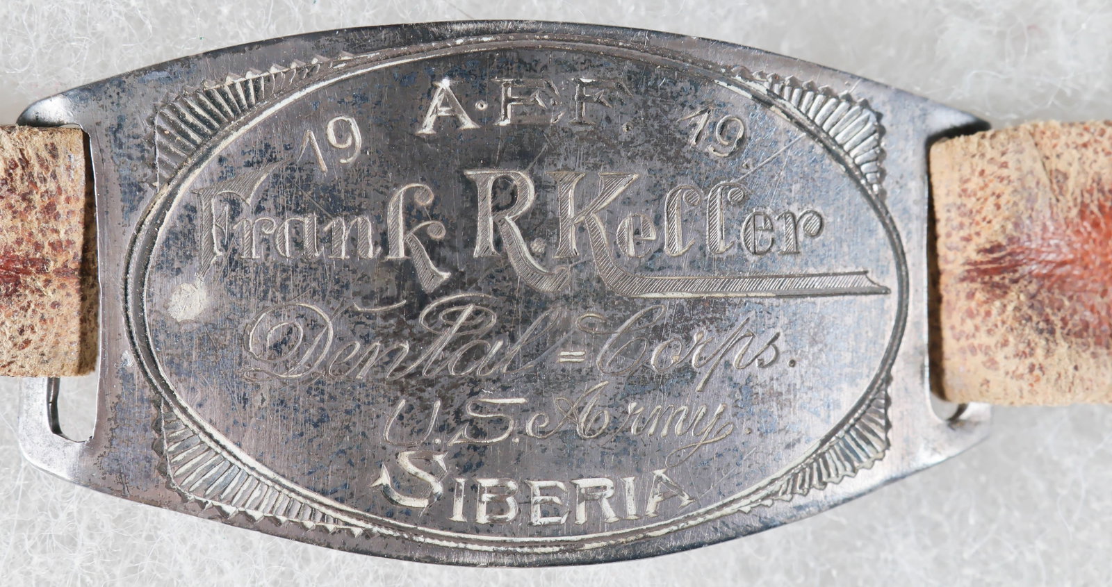1919 AEF SIBERIA ID BRACELET: An unusual World War I relic: a brown leather strap bracelet measuring 8.75 in. with a pin/tang fastener, bearing a 1.75 x .8 in. silver ID tag at middle identifying the wearer as ‘Frank R.
