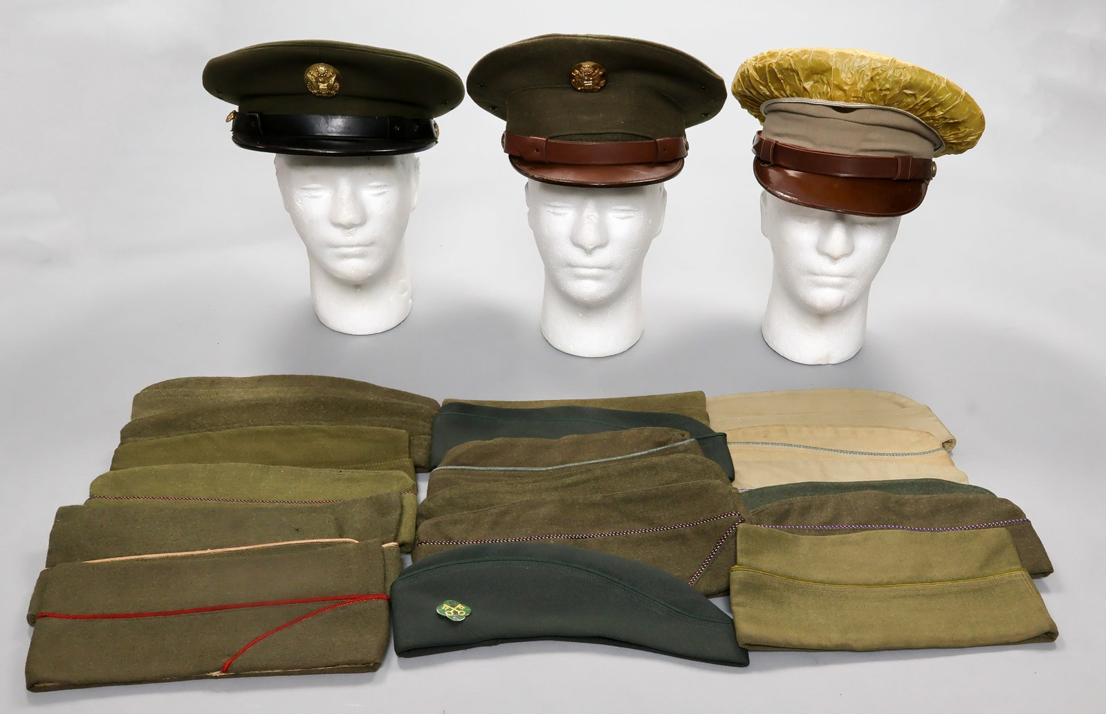 U.S. MILITARY HEADGEAR (21): A good collection of World War II-era and immediately postwar U.S. military headgear, including three U.S. Army officer’s visor caps with round brass cap badges, as well as eighteen overseas or 