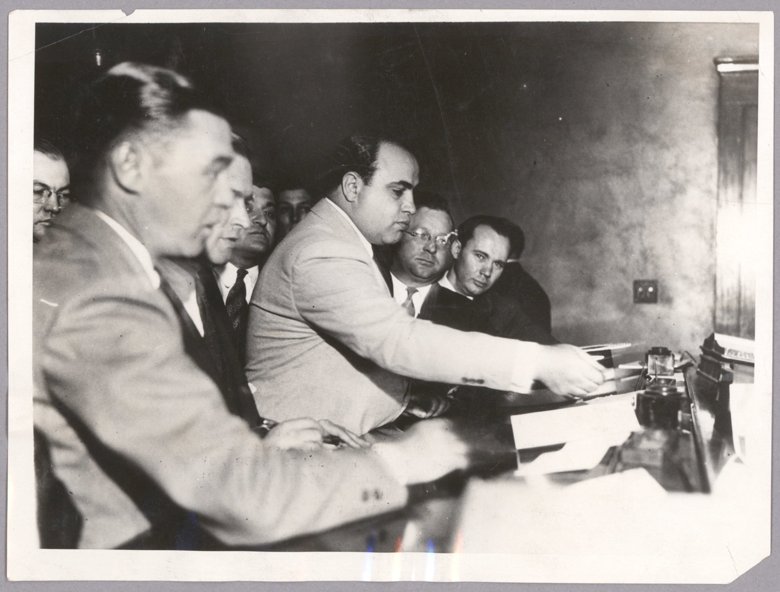 (ALPHONSE CAPONE IS INDICTED ON TAX CHARGES): Excellent original press photograph, 6 x 8 in. b/w, shows Capone with his famous Panama hat before him as he signs his $50,000 bail bond paperwork immediately following his indictment on income tax