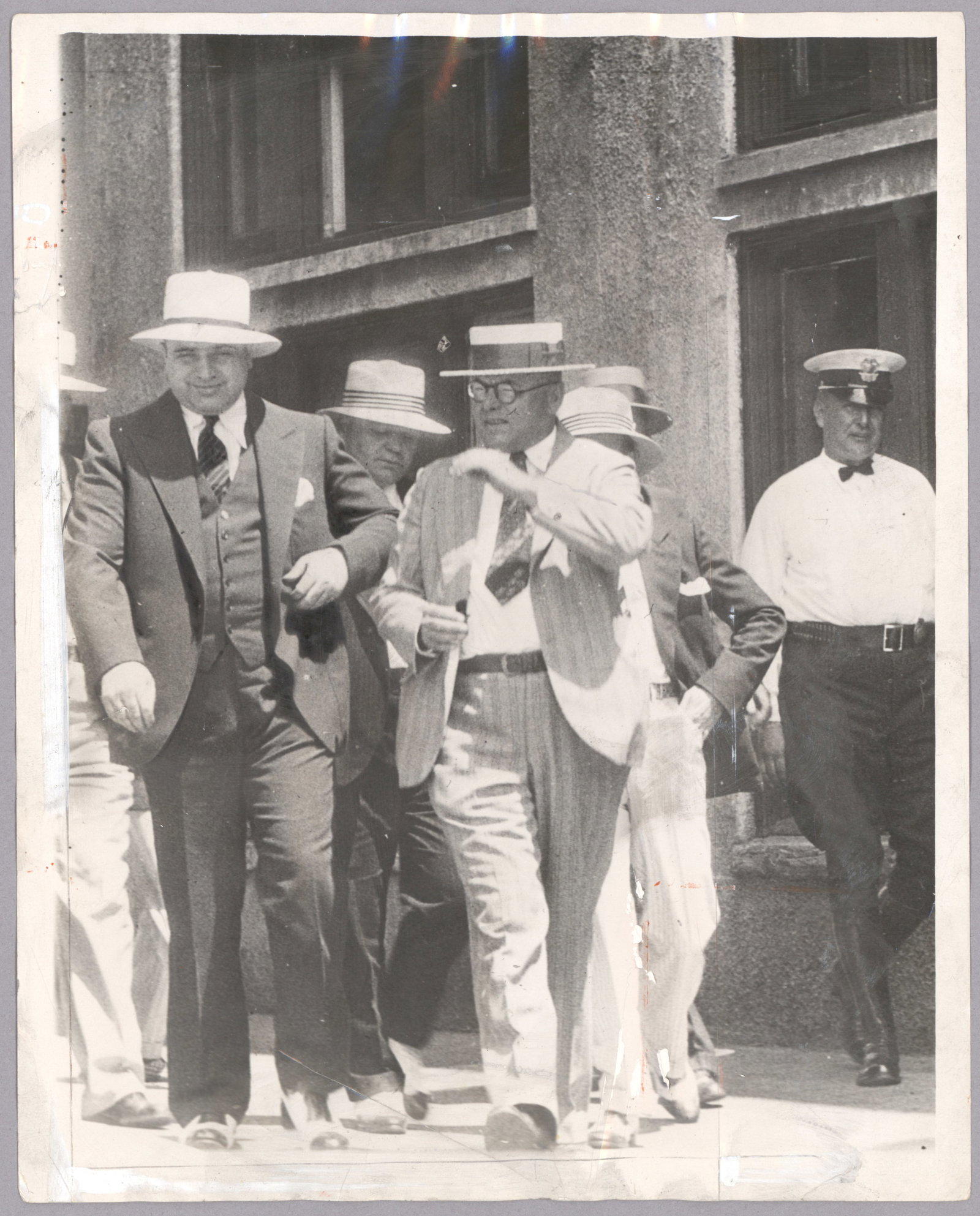 (ALPHONSE CAPONE): An original press photo, 8 x 10 in. b/w, shows Capone in the custody of Miami Police Chief Guy C. Reeves following his arrest there following one of multiple such charges for vagrancy. One use date