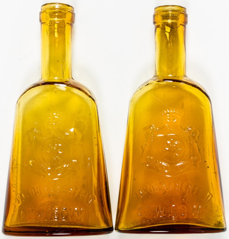 JAKOB HABERFELD LIQUOR BOTTLES FROM AUSCHWITZ: JAKOB HABERFELD LIQUOR BOTTLES FROM AUSCHWITZ Pair of amber glass bottles manufactured at the Jakob Haberfeld vodka and liquor factory at Oswiecim (later Auschwitz) each 4 1/2"" x 2"" bearing in relie