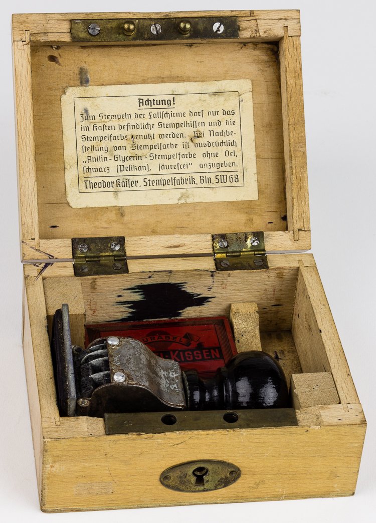 GERMAN PARACHUTE INSPECTOR'S STAMP, INK AND BOX: GERMAN PARACHUTE INSPECTOR'S STAMP, INK AND BOX An odd military relic, a cased German military parachute inspector's stamp with ink pad, the stamp showing german eagle, swastika, date, and inspector n