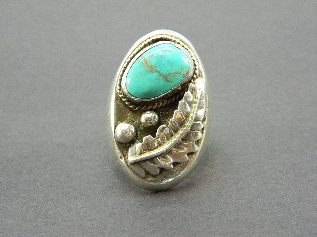 American Indian Sterling Silver & Turquoise Ring: Sterling silver ring with turquoise stone and leaf design on front . Unsigned. Weight 35.1 grams.