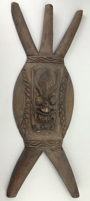 Ifugao Carved Wood Ceremonial Shield.: 32"Lx10.5"W. Philippines, Late 19th/Early 20th century. Features a central mask carving with a grimacing face, associated with a protective spirit, and has trilobal (3-pronged) shape at top and biloba