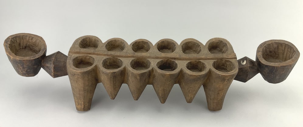 Hand Carved Wood African Mancala Game Board.: 30"Lx6"W. African hand-carved wood Mancala game board, elongated rectangular shape with 14 hollowed-out circular holes for stones or beads, circular form handles to each end, resting on four tapered l