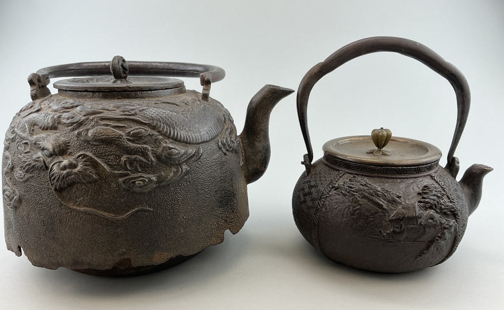 2 Japanese Meiji Cast Iron Tetsubin Kettles.: Measure 8.5 and 13 inches high. Both are likely Meiji period (1868-1912). Larger has embossed cast dragon and tiger motif, smaller has embossed cast cottage and landscape motif. Condition: Good with u
