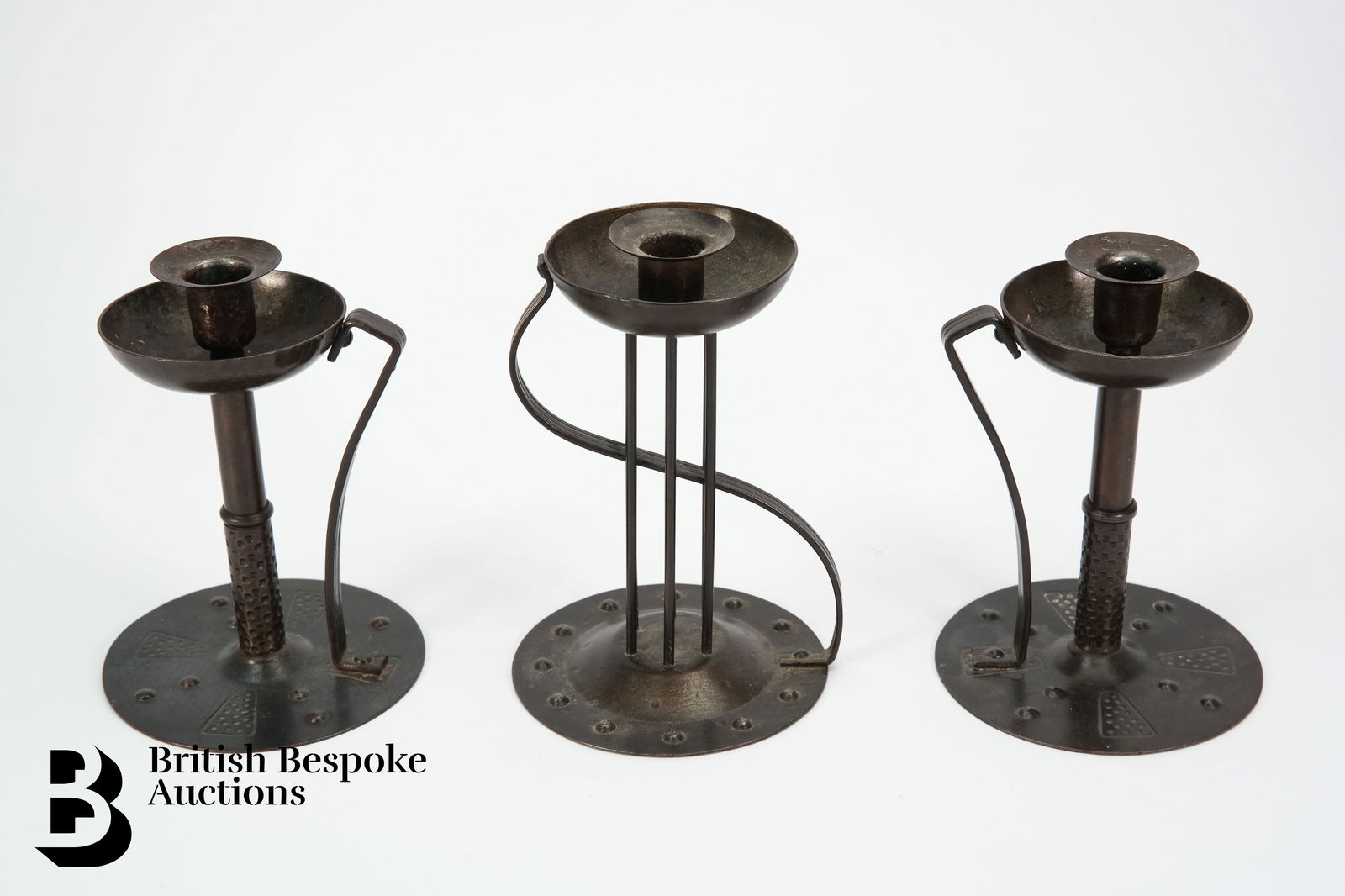 Three Hugo Berger (Goberg) Candlesticks: A pair of Arts and Crafts Hugo Berger, Goberg wrought iron candlesticks, stamped to base, measures approx. 19.5cms h, together with another Arts and Crafts Hugo Berger, Goberg wrought iron candlestick