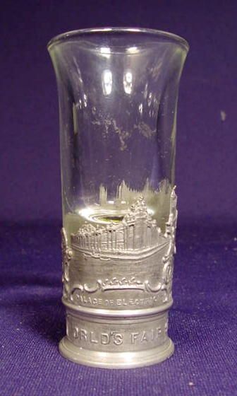 1904 World's Fair Clear Shot Glass: 1904 St. Louis World's Fair clear shot glass in embossed metal base showing Palace, Gardens, Union Station, made in Germany. 3 13/16"T.