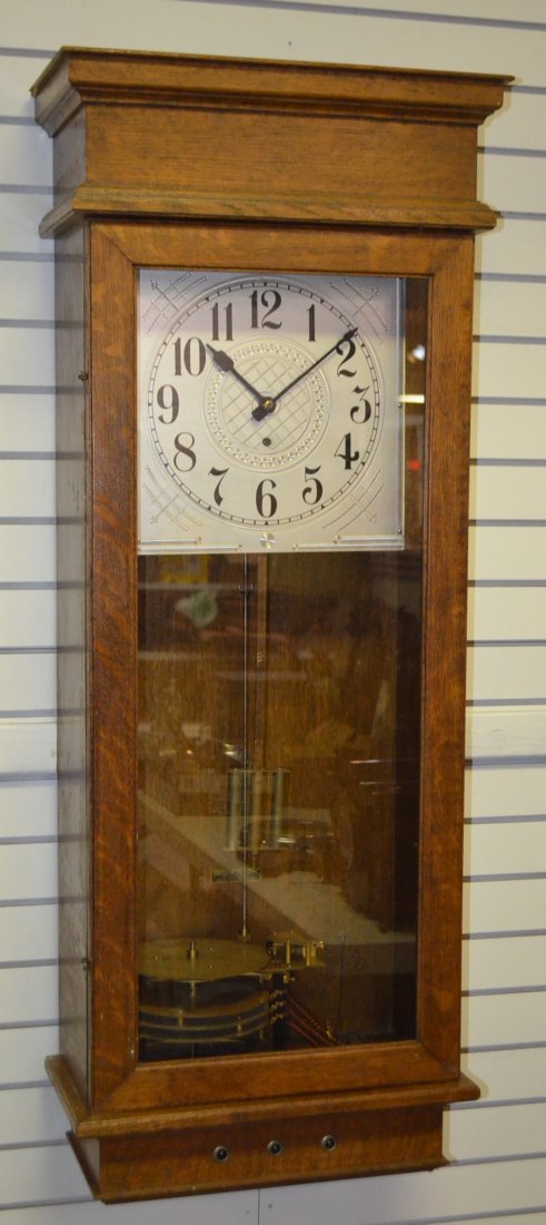 Oak Montgomery Time System Wall Clock: Oak Montgomery Time System Wall Clock: by Hansen Mfg.; pressed tin dial; has pendulum, key and instruction booklet. 48" T. (Small area of case damage on the top left back corner.) Has not been tested,