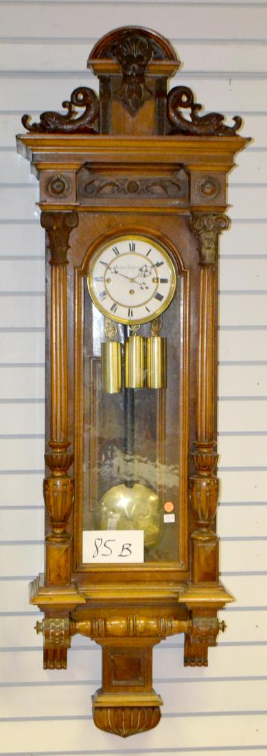 Gustav Gummert 3 Wt. Vienna Wall Clock: Gustav Gummert 3 Wt. Vienna Wall Clock. Carved walnut case, signed 2 piece porcelain dial, brass trim, weights & pendulum, carved dolphins on top crest. Has not been tested. Sells as is, where is. 57"
