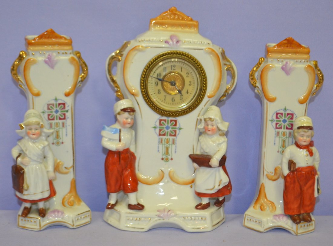 German Porcelain 3 Piece Clock Set: German Porcelain 3 Piece Clock Set, ethicnally dressed children. Set keywind; unsigned case and dial; clock has a boy with a flag and a girl with a boat in front of it; side vases have school boy and