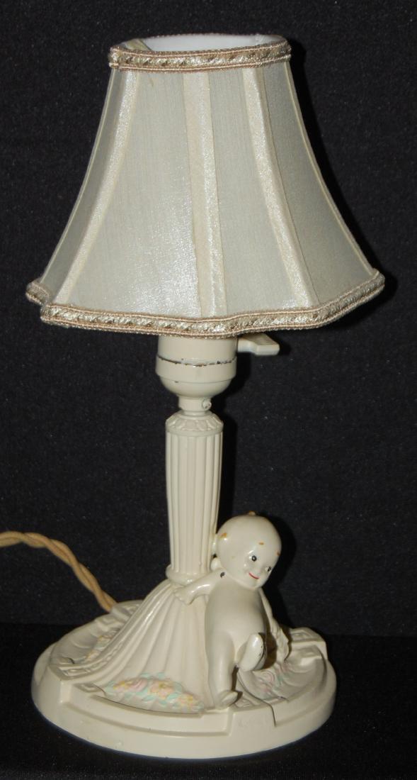 Antique Painted Metal Kewpie Dresser Lamp: Antique Painted Metal Kewpie Dresser Lamp, Electric: Bunderboo reclining against floral embossed lamp post; switch marked Leviton. Modern shade. 13" T Sells as is, where is.