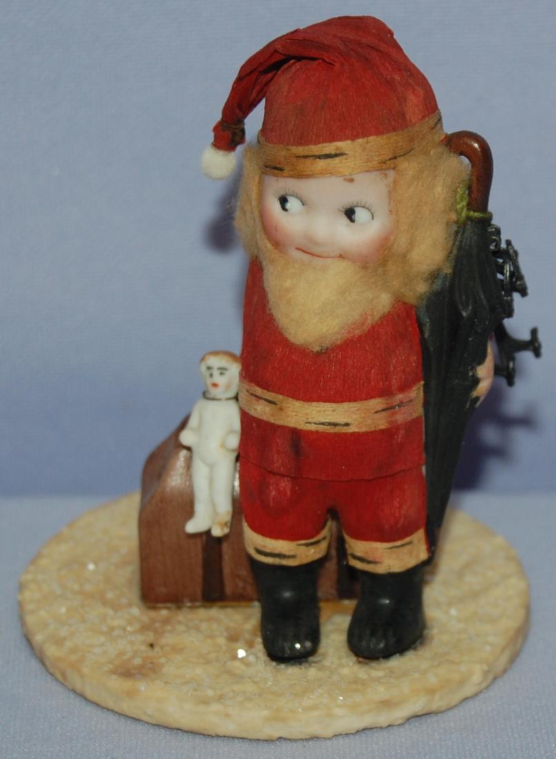 Antique Bisque Kewpie Traveler Dressed as Santa: Antique Bisque Kewpie Traveler Dressed as Santa Claus in a crepe paper suit and hat; attached to a wood base; painted features, 1" frozen Charlotte and metal ice skates attached with wire. 3 1/2" T Se
