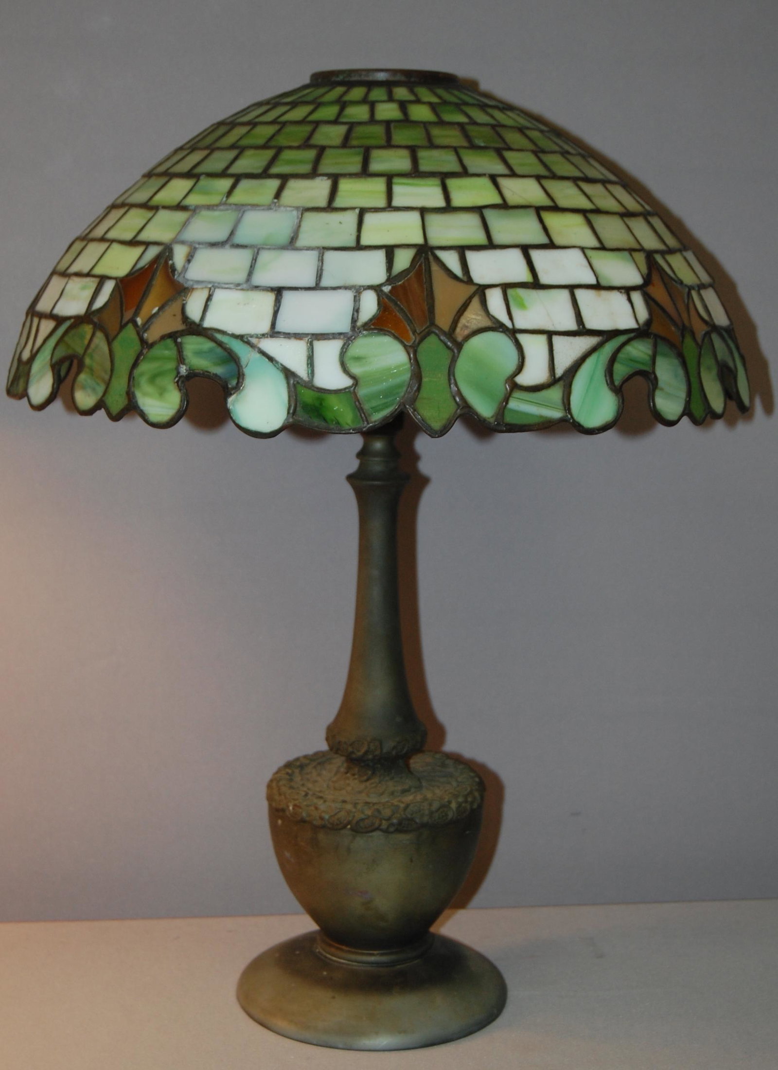 Green Panel Glass Table Lamp. Leaded Geometric shade: Green Panel Glass Table Lamp. Leaded Geometric shade with floral designs. 3 1/2" Top mounting. Multipule damaged sections to the glass and edge area. Weighted iron base marked 1884 on underneith side.