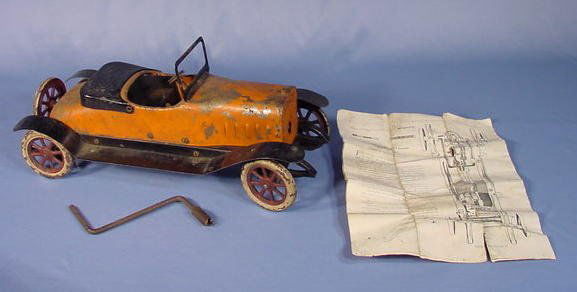 Structo Steel Motorized Toy Roadster Builder: Structo Pressed Steel Motorized Roadster: with instructions, painted orange and black with silver wheels. The motor is hand cranked like an old Model T. The motor is a clock work mechanism with rear e