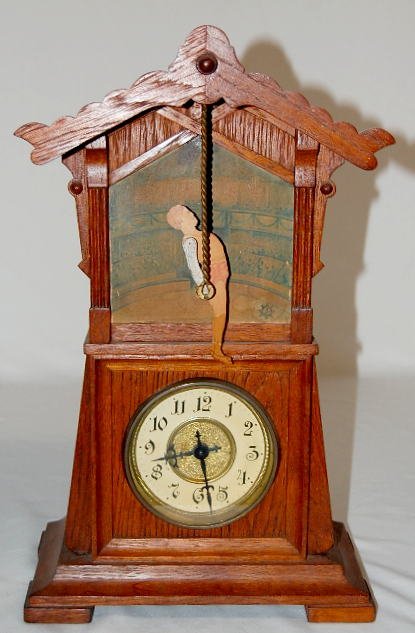 Junghans Man on Trapeze (Acrobat) Clock: Junghans Man on Trapeze (Acrobat) Clock: wooden, 2 story case with 4" dial on the lower half. A paper scene of circus crowd is behind the trapeze man. The movement is not attached to the case. (The ro