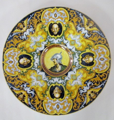 Pottery Wall Plaque, Angels & Faces: Hand Decorated Pottery Wall Plaque, Angels & Faces: hand decorated in vivid colors with angels and the face of a bald man around the wide border. In the recessed center is a man wearing a metal helmet