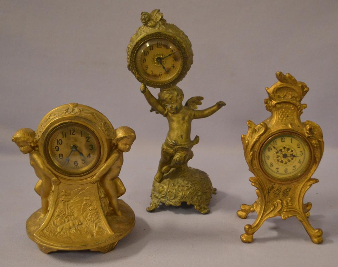 Lot of 3 Novelty Metal Figural Mantle Clock: Lot of 3 Novelty Metal Figural Mantle Clock. 1.) Cherub with wreath on top, gilt center dial, tin can movement, beveled glass. 9 1/2"x4". 2.) Standing children with coon dog scene carved on front, tin
