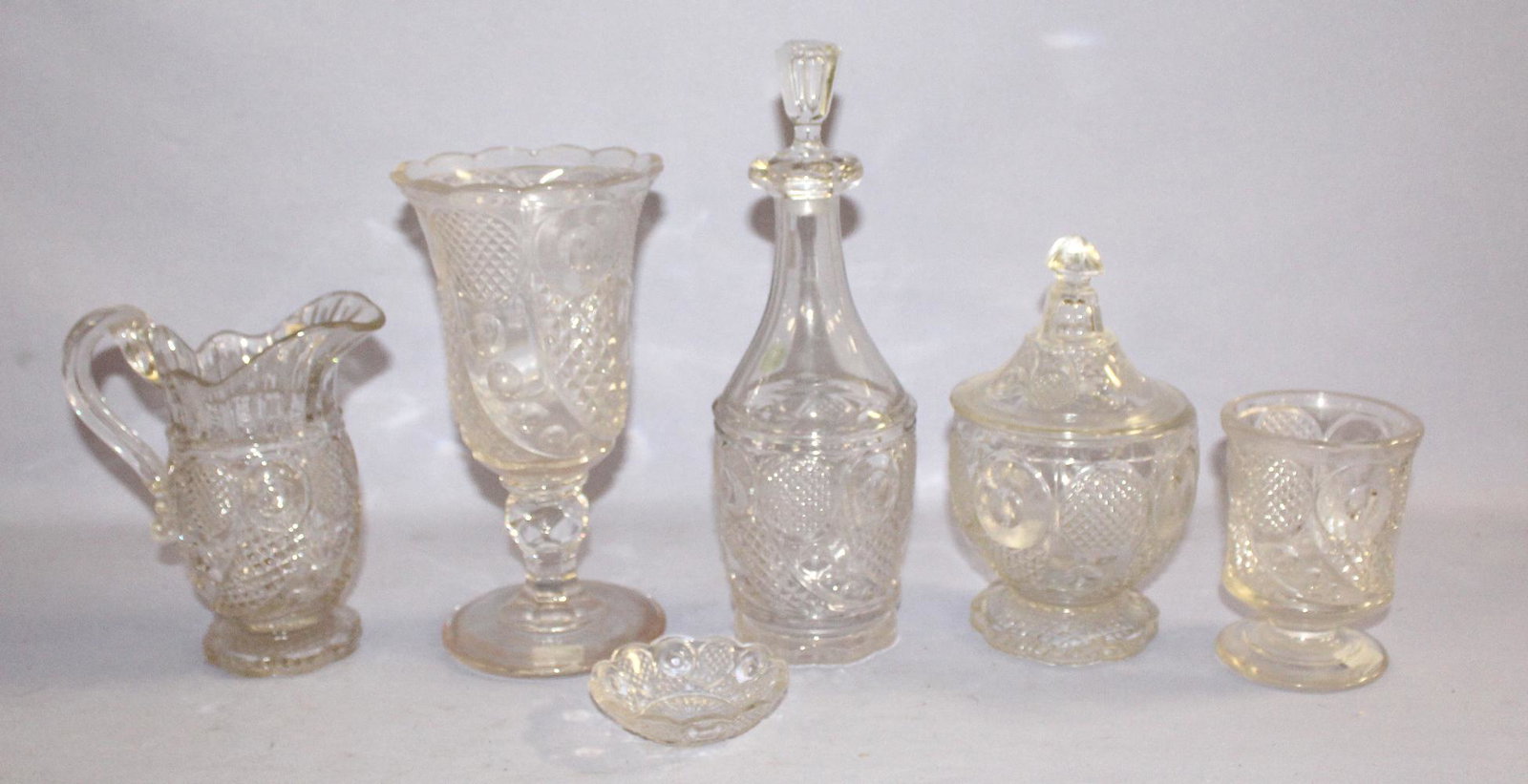 7 Flint Glass "Horn of Plenty" Tableware Collectibles.: 7 Flint Glass "Horn of Plenty" Tableware Collectibles. Celery vase; spooner; cream pitcher, sugar bowl with lid; pint decanter with stopper; round salt. Shelf wear on the bottoms. Tallest 10 3/4"